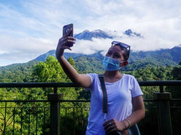 Pengunjung Taman Kinabalu, Gladys Kay Yurus, 23,dari Keningau bergambar dengan berlatarkan Gunung Kinabalu di Taman Kinabalu. Kerajaan Negeri Sabah telah membenarkan pembukaan kawasan pelancongan termasuk semua kawasan Taman-taman Sabah pada kapasiti separuh dan mengikuti prosedur operasi standard (SOP) bagi mencegah penularan COVID-19 bermula hari ini walaupun Sabah masih di bawah Perintah Kawalan Pergerakan Bersyarat (PKPB) sehingga 20 Disember ini.- Foto Bernama