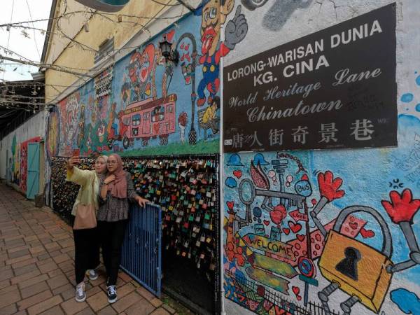 Kelihatan dua orang pengunjung mengambil gambar swafoto di sebuah lorong kecil dihiasi mural yang dinamakan Lorong Warisan Dunia Kampung Cina pada sesi lawatan media ke negeri Terengganu bersama Jabatan Warisan Negara baru-baru ini. - Foto Bernama