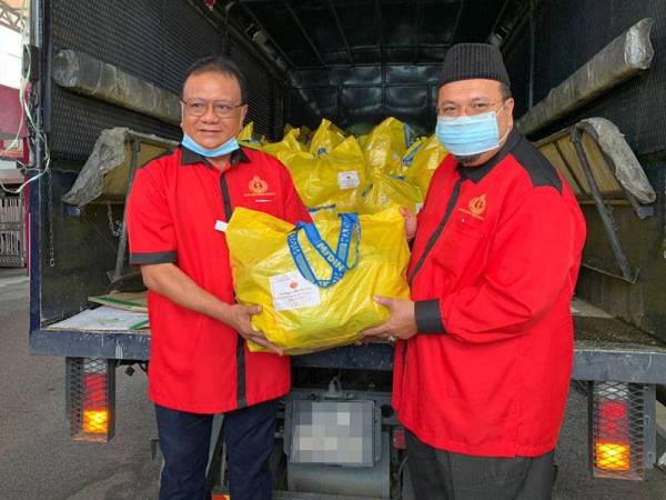 Razali (kiri) menyerahkan bungkusan makanan dan keperluan kepada Abdullah sebagai gimik sebelum pelepasan kenderaan di pekarangan Stadium Sultan Muhammad IV hari ini.