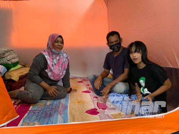Roslina (kiri) dan Mohd Zamri bersama anak mereka Arisya Nur Hazirah, 10, yang menghidap sindrom down kini berpindah ke PPS SK Sri Kelewek selepas kediaman mereka dinaiki air pada Khamis.
