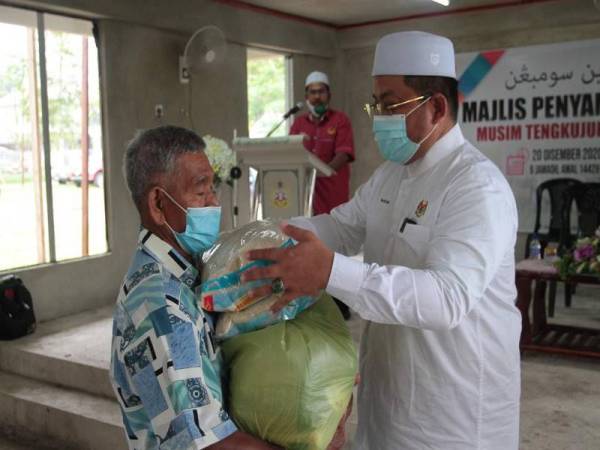 Ahmad Marzuk (kanan) menyerahkan bantuan makanan berikutan musim tengkujuh kepada penerima di DUN Panchor, Kota Bharu di sini hari ini.