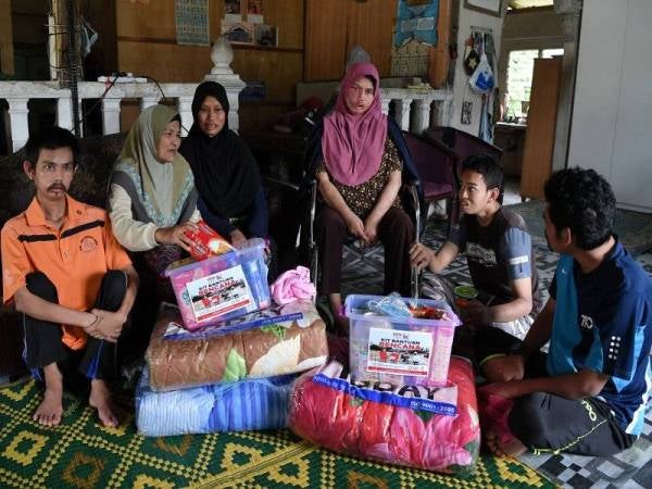 Azizah (dua, kiri) bersama lima daripada enam anaknya yang OKU bisu melihat sumbangan banjir yang diterima ketika ditemui di Kampung Serdang. Foto Bernama