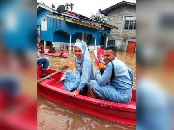Nor Asmira dan pasangannya, Mohamad Farid terpaksa menaiki perahu apabila rumah pengantin perempuan di Kampung Kubang Siput, Kuala Itek, Rantau Panjang dinaiki banjir.