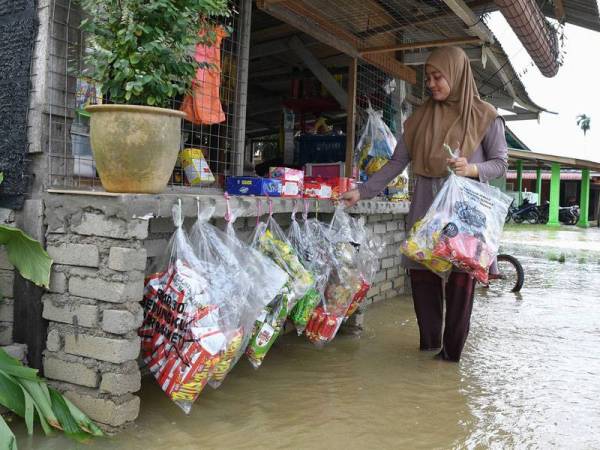 Peniaga Norhayati Harun, 24, menggantung barangan bagi menjalankan operasi perniagaan selepas air banjir mula surut ketika tinjauan di Kampung Bukit Mentok hari ini. - Foto Bernama