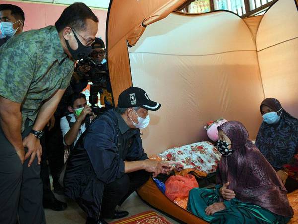 Muhyiddin (dua dari kiri) beramah mesra dengan mangsa banjir ketika melakukan lawatan ke PPS di SK Bukit Mentok hari ini.