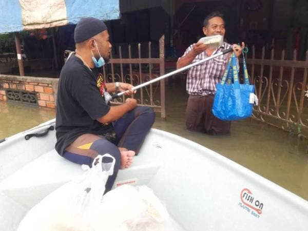 Salah seorang sukarelawan Dapur Darurat Kak Zah mengangihkan makanan menggunakan perahu kepada mangsa banjir di kediaman mereka sekitar pekan Rantau Panjang.