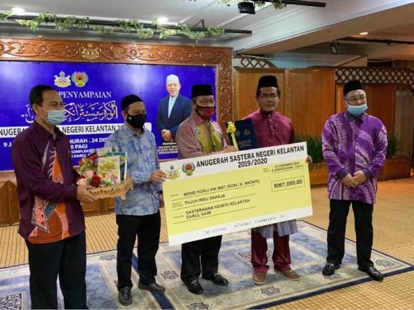 Md Anizam (tengah) menyampaikan replika cek kepada Mohd Rosli Nik Mat atau Rosli K Matari yang dianugerahkan sebagai Sasterawan Negeri Kelantan pada majlis di Dewan Bungan Teratai, Kompleks Kota Darulnaim di Kota Bharu pada Khamis.