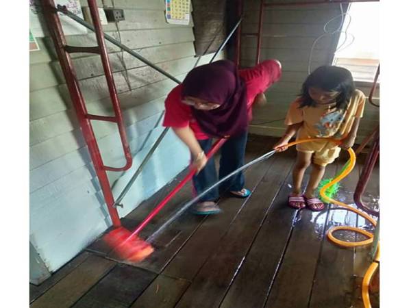 Zamzurina Azhari, 38, bersama anaknya, Zarra Hayfa, 8, membersihkan kesan banjir di rumah mereka di Jalan Sekolah Cina, Rantau Panjang.