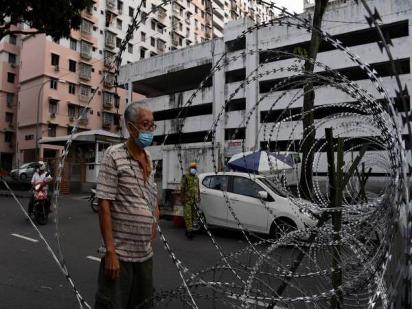 Seorang penghuni flat di Persiaran Paya Terubong Relau memerhatikan kawad duri yang telah dipasang di pekarangan flat berkenaan berikutan pelaksanaan PKPD bermula 7 Disember lalu. Foto: Bernama 
