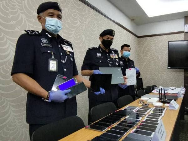 Zainuddin (kiri) menunjukkan telefon bimbit yang dirampas daripada sindiket Macau Scam di Ipoh.