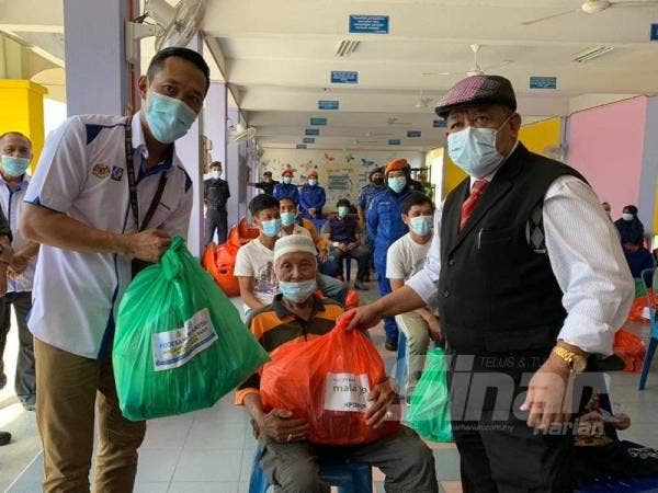 Azanizam (kiri) dan Ketua Jajahan Pasir Mas, Nik Mohamed Nor Nik Ishak (kanan) menyampaikan bantuan kepada seorang penerima pada Program Misi Bantuan Pasca Banjir Pantai Timur di Sekolah Kebangsaan Gual Tok Deh, di sini.
