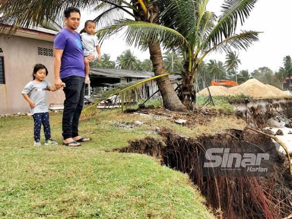 Mohd Afifullah bersama dua anaknya melihat kawasan belakang kediaman mereka di Kampung Pengkalan Maras, di Kuala Nerus yang kini hanya menunggu masa untuk runtuh.