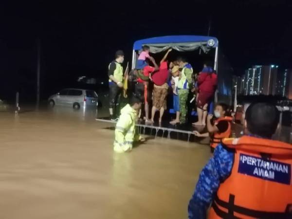 Anggota Jabatan Pertahanan Awam Malaysia memindahkan penduduk yang terjejas akibat banjir di Kampung Kangar Tebrau, Johor Bahru pada malam Sabtu.