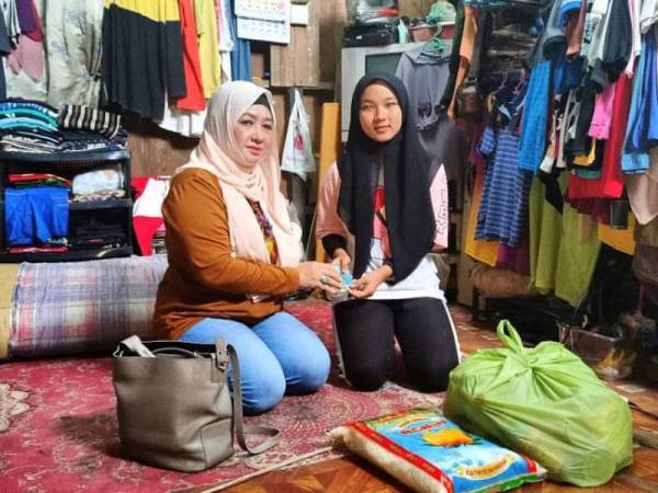 Nur Amalina menerima sumbangan daripada badan bukan kerajaan (NGO) Pertubuhan Cempaka Merah, Asnaf Che Norhayati Mohamed (kiri).
