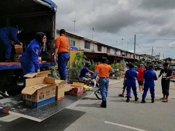 Anggota APM mengagihkan makanan kepada penduduk yang sedang membersihkan rumah mereka selepas banjir surut di Taman Kemang, Kota Tinggi pada Rabu.