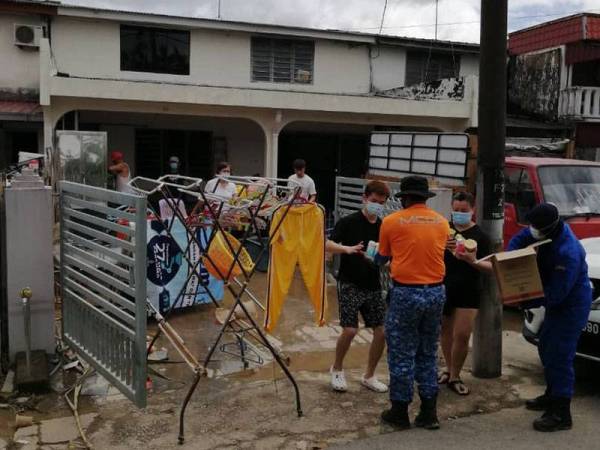 Anggota APM mengagihkan makanan kepada penduduk yang sedang membersihkan rumah mereka selepas banjir surut di Taman Kemang, Kota Tinggi pada Rabu.