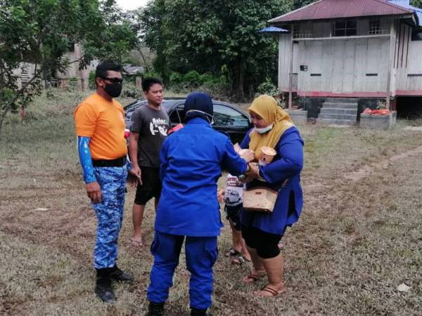 Anggota Angkatan Pertahanan Awam (APM) mengagihkan makanan kepada penduduk yang sedang membersihkan rumah mereka selepas banjir surut di Kampung Kelantan, Kota Tinggi pada Rabu.