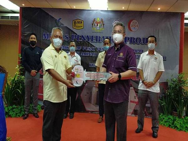 Adham (kanan) menyerahkan replika kunci sebagai simbolik penyerahan pada Majlis Penyerahan Projek Menaik Taraf Pusat Pengumpulan Darah di HSA, Johor Bahru pada Sabtu.