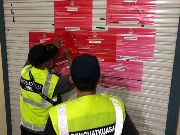 Anggota penguatkuasa DBKL menampal notis di premis yang diserbu.