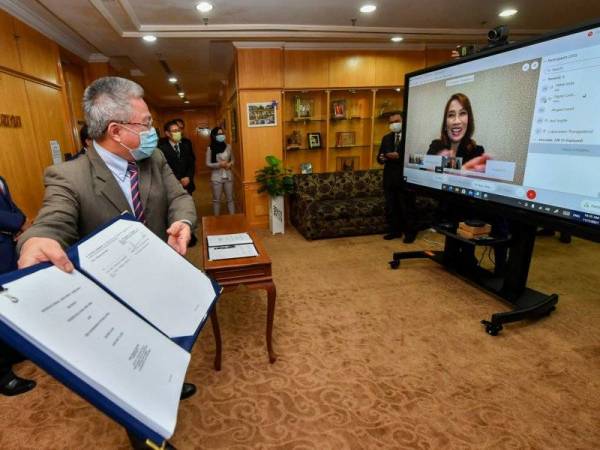 Menteri Kesihatan, Datuk Seri Dr Adham Baba yang mewakili kerajaan Malaysia menunjukkan dokumen perjanjian pembuatan dan pembekalan vaksin Pfizer Covid-19 kepada Pengurus Negara Pfizer Malaysia dan Brunei, Luksanawan Thangpaibool (skrin) selepas menandatanganinya melalui sidang video di Kementerian Kesihatan pada Isnin.
--fotoBERNAMA