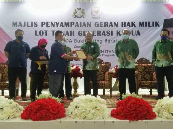 Rasman Ithnain (tiga dari kanan) menyampaikan geran hak milik lot tanah generasi kedua kepada seorang penerima di Felda Bukit Aping Barat Kota Tinggi pada Isnin.