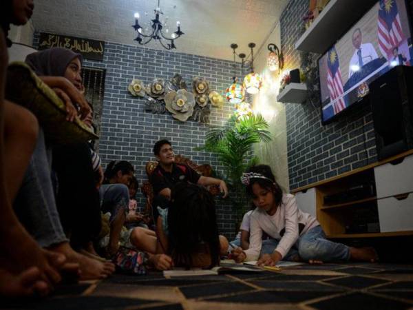 Sebuah keluarga menonton siaran langsung perutusan khas Perdana Menteri, Tan Sri Muhyiddin Yassin menerusi televisyen ketika tinjauan di ibu negara pada Isnin. - Foto Bernama