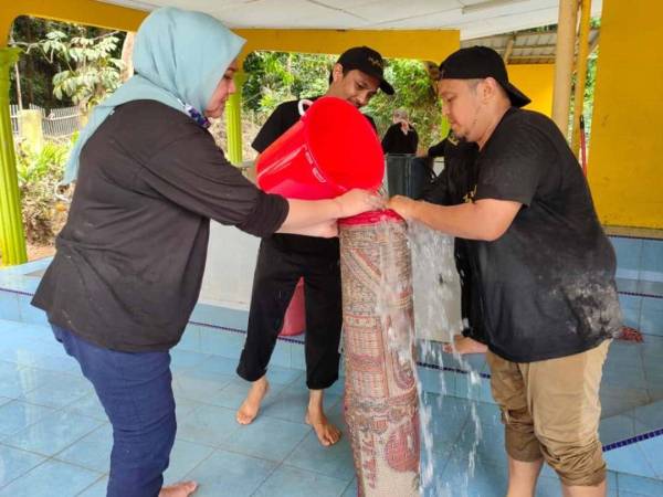 Ruhaidini (kiri) bersama sukarelawan membersihkan sejadah yang terjejas di Majid Kampung Kelola, Jerantut.