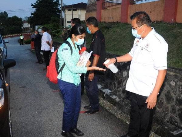 Yahya (kanan) membantu pelajar membersihkan tangan menggunakan cecair pembasmi kuman di luar perkarangan SMK Sultan Ismail Johor Bahru pada Rabu.