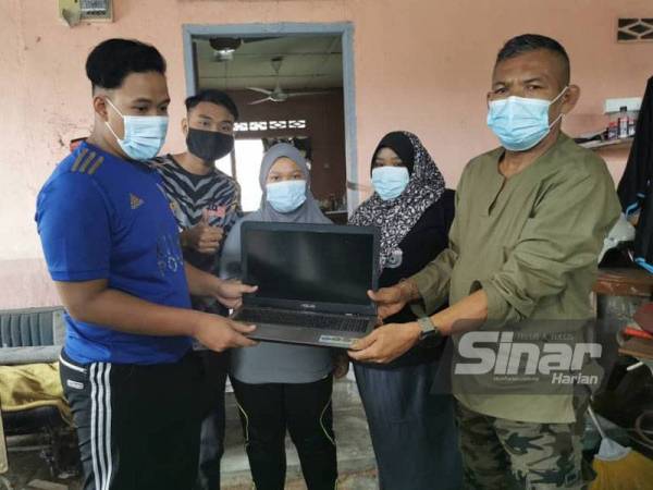 Mohd Yusof menyerahkan komputer riba kepada Muhammad Zulfikar Daniel untuk kegunaan pembelajaraan dia dan adik-adiknya.