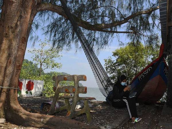 Pelajar Sekolah Menengah Sains Tun Syed Sheh Shahabuddin Bukit Mertajam, Nur Alea Soffiyyah Ahmad Hanif, 16, mengikuti sesi Pengajaran dan Pembelajaran di Rumah (PdPR) menerusi telefon bimbit di tepi pantai Pulau Aman berikutan masalah pencapaian internet yang terhad, ketika tinjauan hari ini.