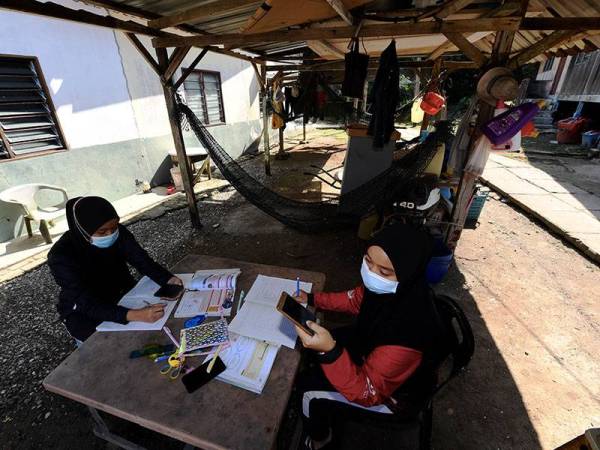 Pelajar Sekolah Menengah Sains Tun Syed Sheh Shahabuddin Bukit Mertajam, Nur Alea Soffiyyah Ahmad Hanif, 16, (kiri) bersama rakan sekelasnya Hanis Syuhada Razali, 16, mengikuti sesi Pengajaran dan Pembelajaran di Rumah (PdPR) menerusi telefon bimbit di dalam bangsal tepi pantai Pulau Aman berikutan masalah pencapaian internet yang terhad.