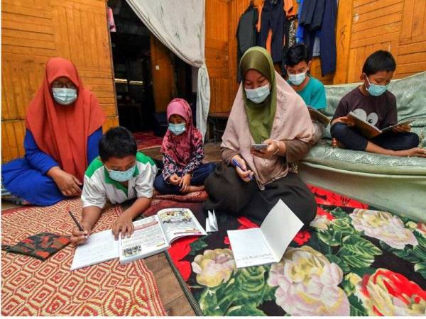 Hasyani Mat Jusoh, 42, (kiri) memperhatikan anaknya Siti Nur Bariah Sidek, 15, (tiga, kanan) mengulang kaji pelajaran kaedah Pengajaran dan Pembelajaran di Rumah (PdPR) secara atas talian sambil adik beradiknya yang lain Siti Nurul Batrisyia, 6, (tiga, kiri), Muhammad Nasrullah, 9, (dua, kiri), Muhammad Naqiuddin, 11, (kanan) dan Mohd Najmuddin, 13, (dua, kanan) menunggu giliran ketika ditemui pemberita di rumah mereka di Kampung Sri Kulim Melor hari ini. - Foto Bernama