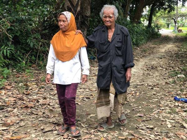 Wan Mohamed memegang bahu isterinya, Fatimah ketika berjalan kaki untuk pulang ke rumah selepas selesai mengambil upah mengurut.