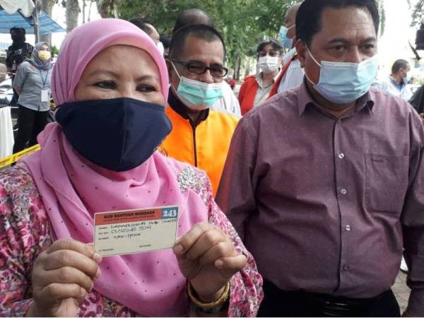 Zaiton (kiri) dan Mohamad menunjukkan kad khas membolehkan gelandangan mengambil makanan disediakan pihak NGO dan sumbangan pelbagai pihak di Laman Tun Sri Lanang, Johor Bahru.