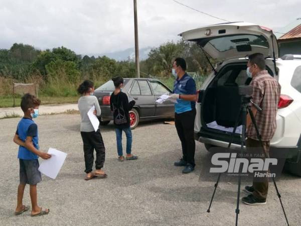 Murid orang asli merebut peluang beratur untuk mendapat bahan PdPR dihantar guru ke kampung mereka.