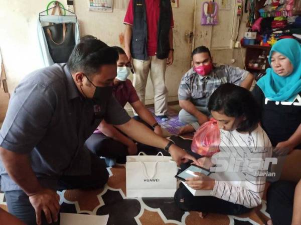 Muhd Akmal Fawwaz (kiri) menunjukkan sesuatu di dalam tablet yang disumbangkan kepada Nor Hazira sekeluarga di Kampung Padang, Jalan Pegawai, Alor Setar pada Ahad.