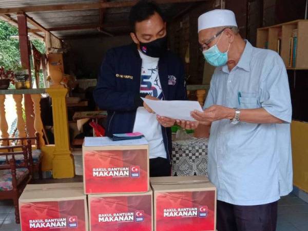 Onn Hafiz (kiri) menerangkan cara pengagihan bantuan kepada Muhamad Jakorni ketika mengagihkan bekalan makanan, baucar dan wang tunai di Kampung Chokro, Renggam, Kluang pada Khamis.