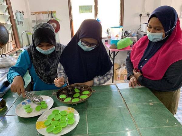 Dua adiknya iaitu, Najwa (tengah) dan Nasreen (kiri) membantu menyusun kuih cara yang dibuat Aimi Nazerah (kanan) di rumahnya di Melor.