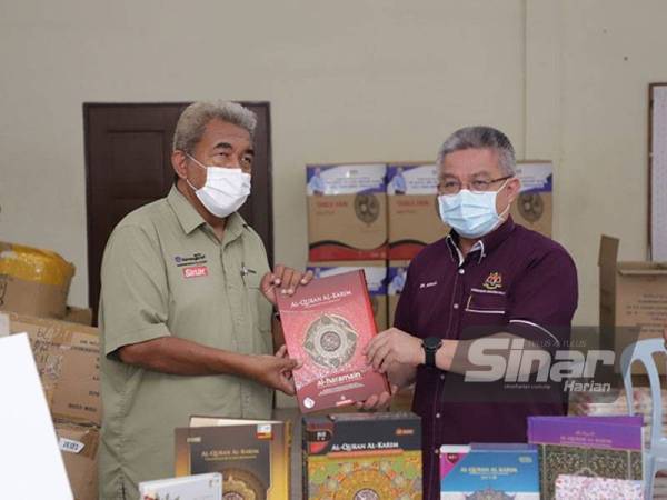 Adham ( kanan ) menerima Al-Quraan dari Sekteriat Wakaf Al-Quran Warisan Ummah Ikhlas (WUIF) yang disampaikan Hashim (kiri) di Balai Raya Taman Kota Jaya, Kota Tinggi di sini pada Ahad.