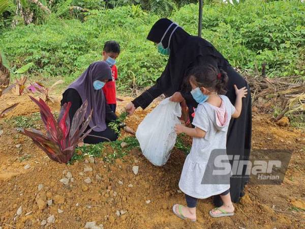 Farah Nabila (duduk, kiri) bersama ibu dan anak-anaknya menabur bunga di pusara arwah di Tanah Perkuburan Islam Bukit Cemerlang, Klang pada Rabu.