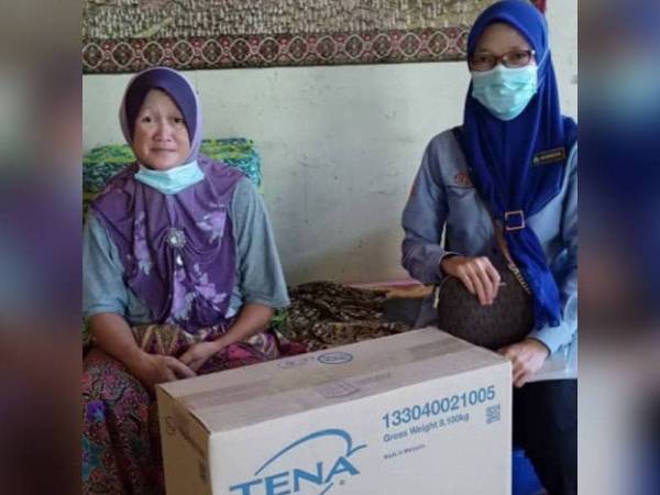 Pegawai Skuad Perkeso Prihatin (SPP) Kluang, Norfaizah Mohdi (kanan) menyerahkan bekalan lampin pakai buang kepada Noryati di kediamannya di Kampung Tanjung, Renggam, Kluang.