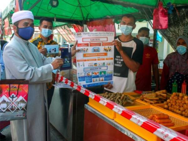 Nik Muhammad Zawawi (kiri) menyampaikan risalah mengenai ancaman Covid-19 kepada seorang peniaga kecil, Puteh Mohd Khairulaizam Mohd Yusof, 41, (tiga dari kanan) pada Program 'Info On Wheels' (Low) Kempen Pematuhan SOP Covid-19 Daerah Pasir Puteh, di Bandar Baru pada Rabu. - FOTO: BERNAMA