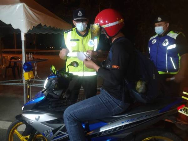 Ahmad Shukri (kiri) ketika memeriksa borang kebenaran rentas negeri seorang penunggang motosikal di Tol Alor Setar (Selatan) pada Khamis.