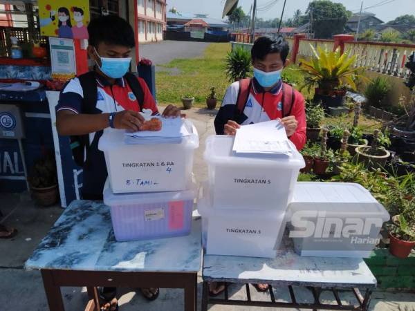 Dari kiri, Mohd Aziq dan Mohd Aliff mengambil bahan pembelajaran yang disediakan guru di pondok kawalan keselamatan di SMK Sri Perhentian.