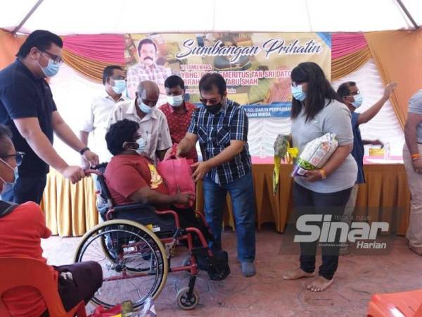 Ibrahim (tengah) menyerahkan sumbangan Yayasan Minda kepada salah seorang penerima bantuan sambil diiringi Sara (kanan) di Pusat Komersil Seksyen 7, Shah Alam pada Sabtu.