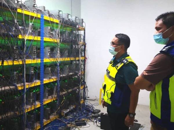 Agus Salim (kiri) bersama pegawainya memeriksa mesin bitcoin yang dirampas pihaknya dalam serbuan di Sabak Bernam pada Ahad.