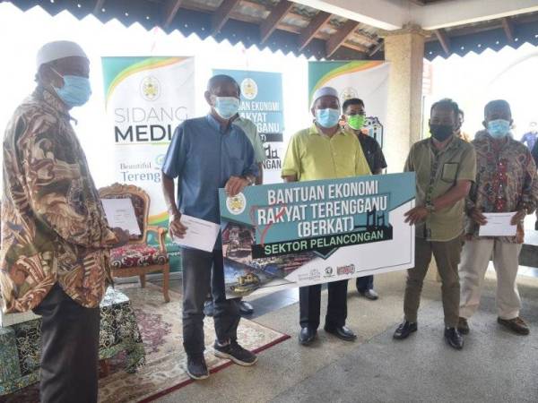 Ariffin (tiga dari kiri) menyerahkan bantuan kepada penerima pada Program Bantuan Ekonomi Rakyat Terengganu (Berkat) bagi sektor pelancongan di jeti bot penambang, Pasar Payang, Kuala Terengganu pada Selasa.