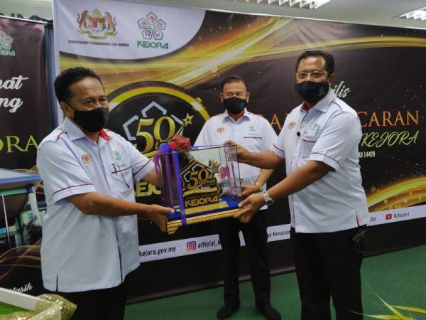 Abdul Rahman (kanan) menerima logo sambutan jubli emas Kejora dari A Jalil ( kiri) di Bandar Penawar pada Khamis.