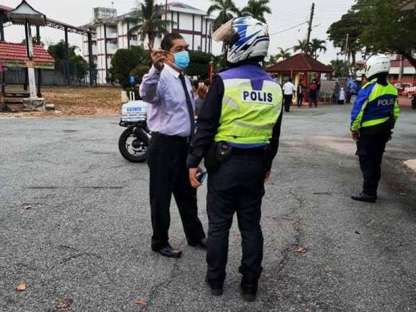 Guru besar SK Haji Mohd Shariff, Mahmuzir Osman (kiri) memberi penerangan ringkas kepada anggota polis yang membuat pemantauan pematuhan SOP di sekolah itu.