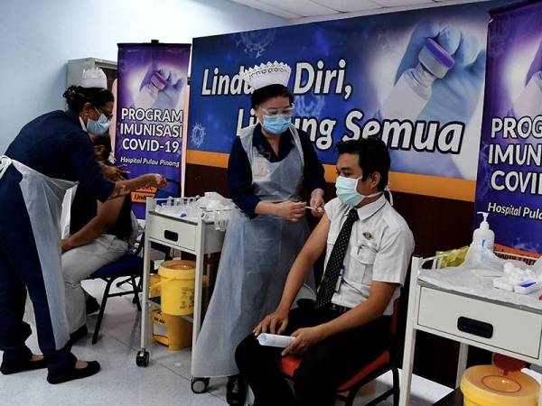 Penolong Pegawai Perubatan, Amirul Aziz Abd Malek (kanan) menerima suntikan dos pertama vaksin Covid-19 di Pusat Pemberian Vaksin Covid-19 , Hospital Pulau Pinang HPP hari ini.